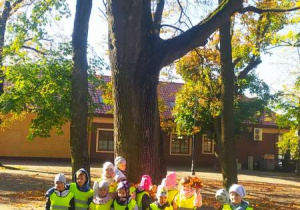 Dzieci stoją przy jesiennym drzewie.