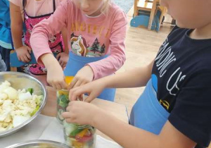 Dzieci wkładają do słoików pokrojone warzywa: kalafior, cukinię, paprykę, cebulę, ogórki, które zostaną zalane solanką.