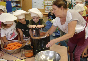 Dzieci wraz z nauczycielką wyciskają sok z marchewki przy użyciu sokowirówki.