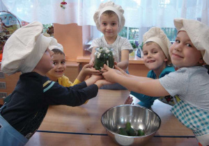 Pięcioro dzieci z uśmiechem pokazują gotowy słoik z ogórkami do wlania wody z solą.
