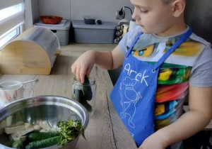 Chłopiec wkłada ogórki do słoika.