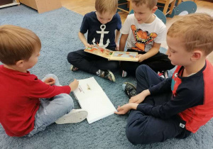 Dzieci siedzą na dywanie i oglądają ilustracje w książkach o misiach.