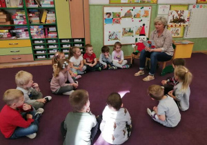 .Dzieci siedzą na dywanie i słuchają opowiadania czytanego przez nauczyciela.la