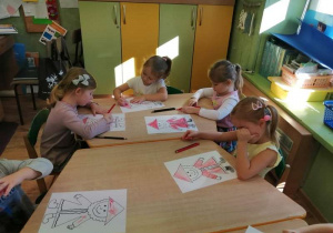 Dzieci siedzą przy stoliku i kolorują postać krasnala Hałabały.