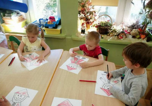 Dzieci siedzą przy stoliku i kolorują postać krasnala Hałabały.