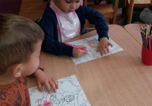 Dziewczynka i chłopczyk siedzą przy stoliku i kolorują obrazki.