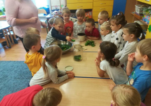 Dzieci zgromadzone wokół stołu, chłopiec wkłada ogórka do słoika