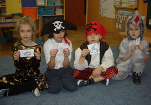 Czwórka przebranych dzieci (Czarodziejka, dwóch piratów i wilk) trzymają karteczki z obrazkami.