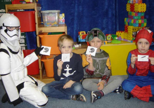 Czwórka przebranych dzieci (Szturmowiec, Diabełek, Boba Fett i Spider-man) trzymają karteczki z obrazkami.