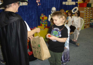 Chłopiec losuje klocek z papierowej torby, którą trzyma Pani Wróżka.