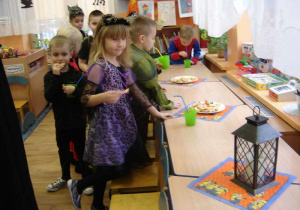 Przebrane dzieci częstują się ciasteczkami ułożonymi na talerzach a na pierwszym planie dziewczynka w stroju czarodziejki.