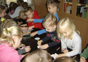 Grupa dzieci koloruje kredkami kontury aniołków i bombek.