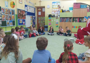Dzieci siedzą w kole i słuchają opowiadania czytanego przez Mikołaja.
