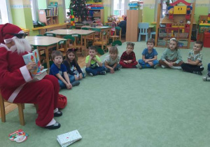 dzieci siedzą w kole, a Mikołaj pokazuje dzieciom książkę o Krasnalu Hałabale.