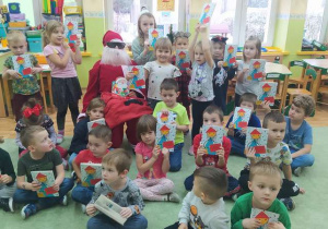 Zdjęcie grupowe z Mikołajem, dzieci prezentują otrzymane książeczki.
