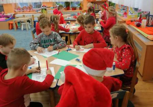 Dzieci siedzą przy stolikach i kolorują sylwetę Mikołaja.