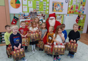 Dzieci pozują z Mikołajem, trzymając w rękach prezenty.