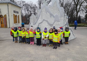 Grupa dzieci stoi przy ozdobie zimowej w parku