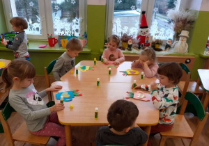 Grupa dzieci przy stolikach wykonuje laurki z gotowych elementów.
