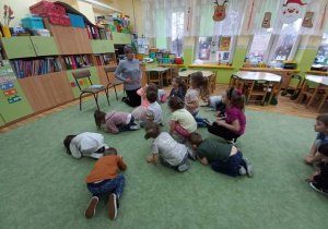 Dzieci siedzą na dywanie, pani bibliotekarka czyta opowiadanie.