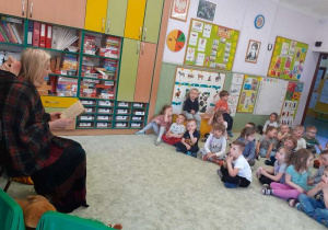 Dzieci siedzą na dywanie słuchają opowiadań o krasnalu czytanych przez aktorkę.