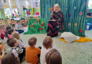 Dzieci siedzą na dywanie, aktorka inscenizuję czytane fragmenty kukiełką krasnala.