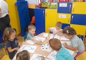 Dzieci przy stoliku malują farbami kontur worka