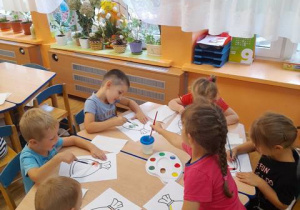 Dzieci przy stoliku malują farbami kontur worka