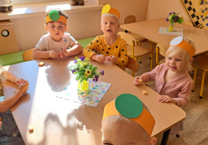 Dzieci w opaskach na głowach z kółeczkami siedzi przy stoliku i jedzą ciastka oraz gumy mamby.