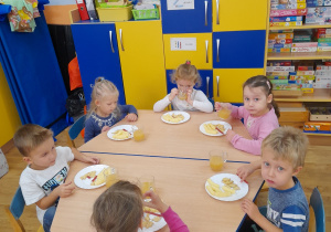 Grupka dzieci spożywa słodycze przy stole.