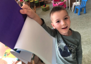 Uśmiechnięty chłopiec trzyma w dłoni zeszyt papierów kolorowych.