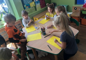 Dzieci kolorowymi listkami ozdabiają wizerunki Pani Jesieni.