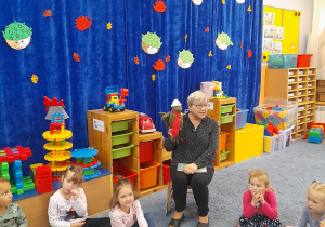 Nauczycielka siedzi trzymając w ręce wróbelka, wokół na dywanie siedzą dzieci.