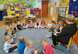Nauczycielka siedzi trzymając w ręce wróbelka, wokół na dywanie siedzą dzieci.