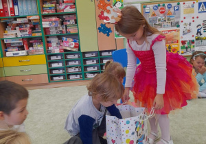 Dziewczynka w koronie i kolorowej sukni częstuje dzieci cukierkami.