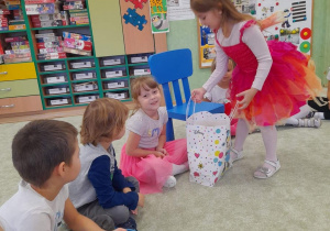 Dziewczynka w koronie i kolorowej sukni częstuje dzieci cukierkami.