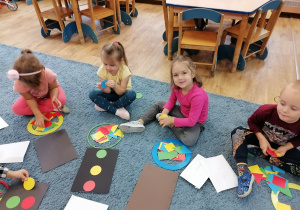 Dzieci na dywanie układają sygnalizator świetlny za pomocą figur geometrycznych.