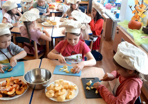 Dzieci w czapkach kucharskich przygotowują sałatkę owocową.