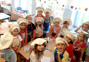 Dzieci pozują do zdjęcia w czapkach kucharskich.