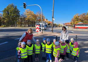Grupa dzieci z paniami na skrzyżowaniu ulicznym
