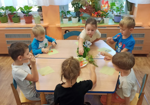 Dzieci siedzą na krzesłach, przy stole i degustują warzywa ułożone na talerzu.