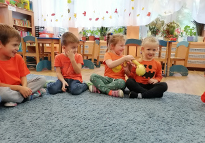 Dzieci siedzą na dywanie i sprawdzają dynie wykorzystując zmysły.