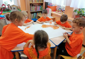 Na stolikach rozłożone duże arkusze papieru , dzieci malują farbami szablony dyni.
