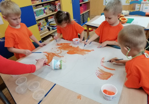 Na stolikach rozłożone duże arkusze papieru , dzieci malują farbami szablony dyni.