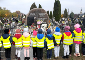 Dzieci stoją tyłem, patrzą na zbiorową mogiłę żołnierzy i ofiar II Wojny Światowej.