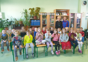 Grupa dzieci siedzi na krzesłach w bibliotece.