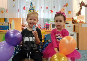 Nasi jubilaci Alicja i Leon siedzą na krzesełkach, trzymając balony.
