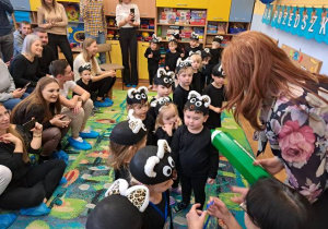 Dzieci w strojach kotków są pasowane na Przedszkolaka dużą zieloną kredką przez Panią Dyrektor