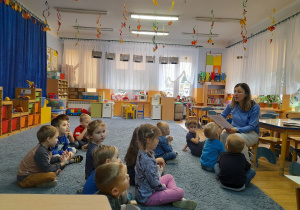 Dzieci siedzą i słuchają wiersza czytanego przez nauczycielkę.