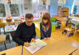 Autor podpisuje dziewczynce książkę.